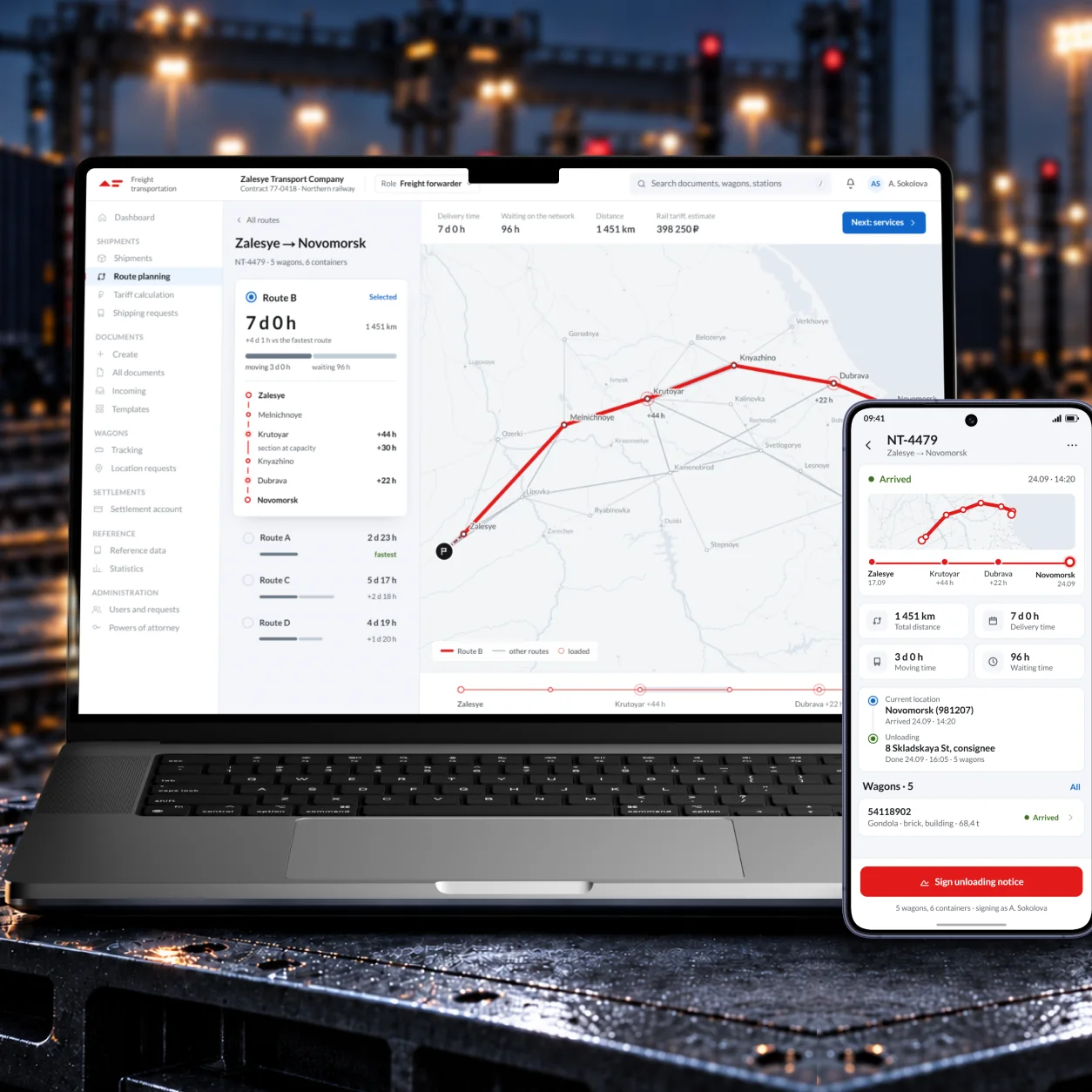 The freight platform on a laptop and a phone at a rail yard at dusk: route B planned across the rail network on the laptop, and on the phone the arrived shipment with its unloading notice to sign.